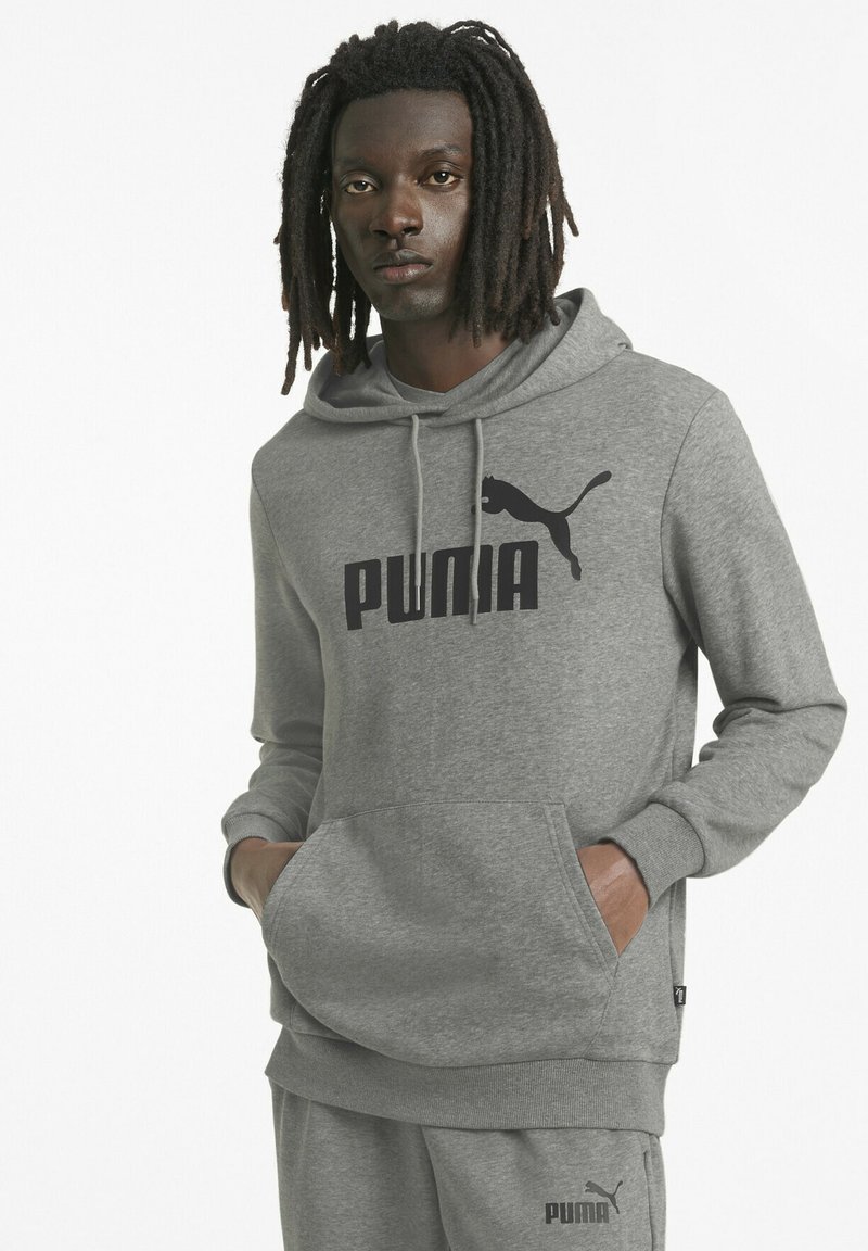 Sudadera gris hecha de un tejido suave que cuenta con un bolsillo tipo canguro, puños acanalados y un gran logo negro de Puma en el frente.