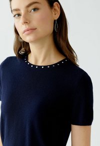 Navyblauer Kurzarmpullover mit rundem Ausschnitt, verziert mit kleinen silbernen Nieten. Weiche Textur mit schmaler Passform und sauberem Design.