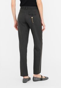 Pantaloni grigi a righe con un design aderente, dotati di una tasca posteriore con bottone e un dettaglio con zip dorata. Indossati con ballerine nere.