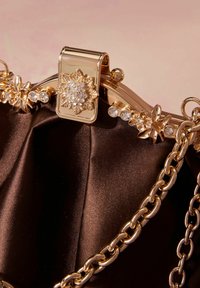 Close-up of a brown satin purse with gold floral clasp decorated with clear crystals and a gold chain strap.