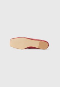 Chaussure plate en cuir rouge avec un dessus lisse, un bout carré et une semelle en caoutchouc beige. La semelle dispose d'une texture antidérapante pour une meilleure durabilité.