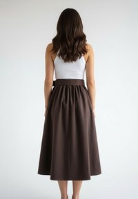 Brązowa spódnica do kolan z plisami i szerokim pasem. Noszona na białym topie na ramiączkach, ukazująca gładką tkaninę i starannie wykonaną konstrukcję.