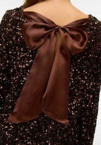 Rudas blizgučiais nusagstyta suknelė su atlasiniu kaspinu gale, turinti gilų iškirpimą ir tekstūruotą paviršių, sukuriantį blizgesio efektą.