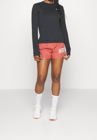 Svart långärmad tröja och röda Nike-shorts, vita sneakers med rosa sulor och vita strumpor med svarta detaljer. Enkel design och sportig stil.