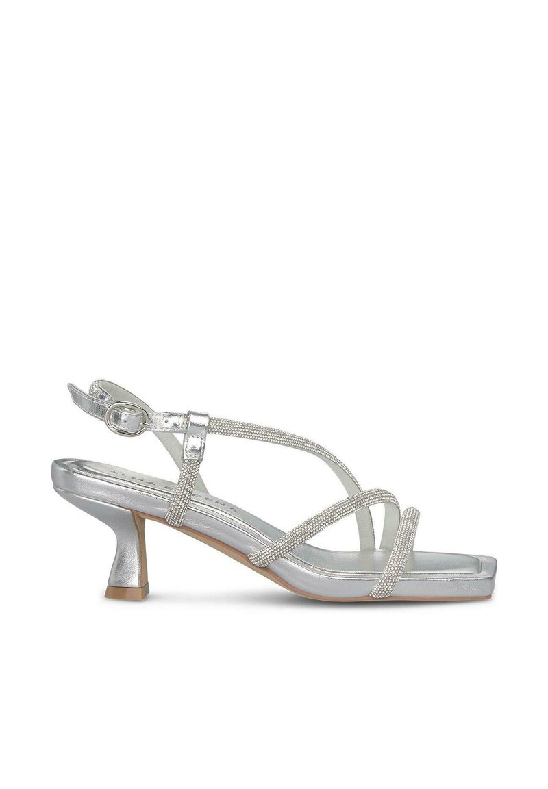 Zilveren sandalen met hakken van een glanzend materiaal, met kruisbanden en een geconfigureerde accent. Vierkante neus en een gematigd taps toelopende hak.