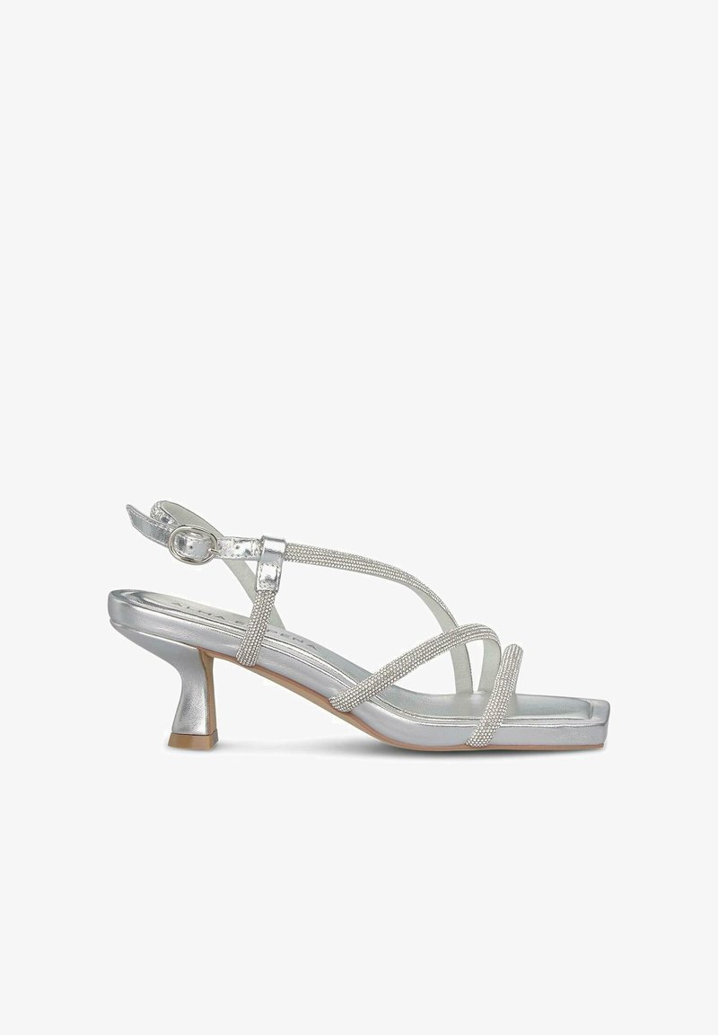 Silberne Sandalen mit Absatz aus glänzendem Material, mit überkreuzten Riemen und einer strukturierten Akzentuierung. Quadratfuß und ein moderat zulaufender Absatz.