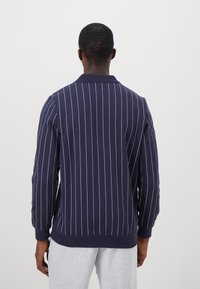 Marineblå sweatshirt med lange ærmer og lodrette hvide striber, der har en krave og ribbede manchetter. Bagvinduet fremhæver et rent, klassisk design.
