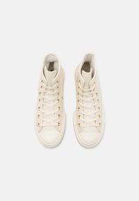 Sneakers high-top color crema realizzati in pelle con occhielli dorati, lacci bianchi, punta arrotondata e superficie texturizzata.