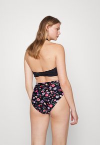 Top de biquíni preto com design halter, combinado com parte de baixo de cintura alta apresentando um padrão floral colorido sobre um fundo escuro.