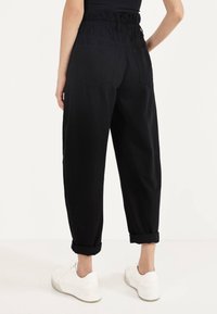 Svarta byxor i bomullsblandning med en samlad elastisk midja, uppvikta benslut och två bakfickor. Matchas med vita sneakers.