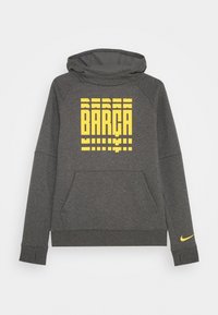 Sudadera gris con un bolsillo frontal, que presenta un gráfico amarillo de "BARÇA". Incluye capucha y un pequeño logo amarillo de Nike en la manga.