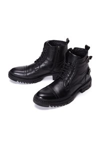 Botas tobilleras de cuero negro con un acabado texturizado, que presentan cordones, cremalleras y suelas robustas con un pronunciado patrón de agarre.