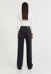 Jean en denim noir taille haute avec une silhouette à jambes larges, ourlet brut, et deux poches arrière. Le matériau a une texture lisse.