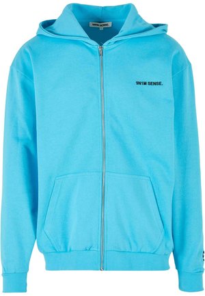 Šviesiai mėlynas užtrauktuku užsegamas džemperis, pagamintas iš minkštos medžiagos. Jame yra priekinė kišenė, gobtuvas ir maža juoda logotipas kairėje krūtinės pusėje.