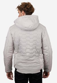 Chaqueta acolchada de color gris claro con capucha, que presenta una textura acolchada hexagonal, puños elásticos y bolsillos laterales. Diseñada para proporcionar calidez y comodidad.