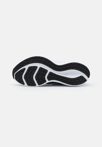Suela de zapato deportivo en blanco y negro con goma texturizada para mejor agarre, que presenta un diseño ondulado y una banda de rodadura con patrón para mayor tracción.