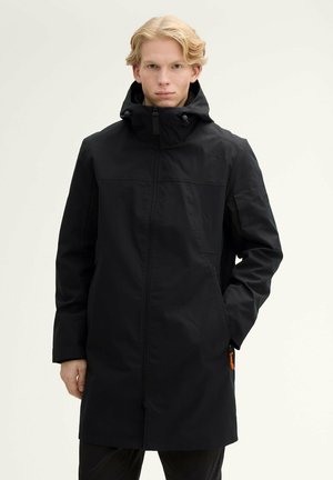 Manteau imperméable noir avec capuche, fermeture éclair à l'avant et poches. Présente un design minimaliste et un tissu durable, adapté pour une utilisation en extérieur.
