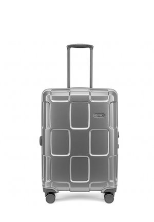 Valise rigide argentée avec quatre roues, une poignée télescopique et un motif géométrique sur le devant, étiquetée « Epic » en haut à droite.