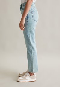 Lichtblauwe denim straight-leg jeans met een klassiek vijf-pocket ontwerp, zichtbare stiksels en minimale slijtage. Draagt met beige en witte sneakers.