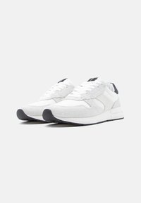 Białe buty sportowe wykonane z teksturowanego materiału, z sznurowaniem, wyściełanym językiem oraz czarnym akcentem na pięcie. Gumowa podeszwa.