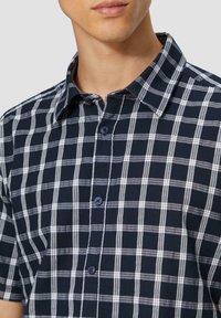 Korte mouw geruite shirt in marineblauw, wit en lichtgrijs. Voorzien van een button-down kraag en donkere knopen. Geweven stof met een zichtbaar ruitpatroon.