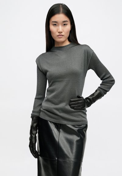 Szürke textúrált pulóver magas nyakkal, sima fekete bőrgömbökkel párosítva. A modellen fekete bőrszoknya van.