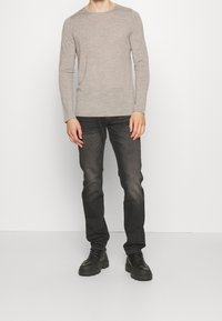 Hellgraues Langarmhemd aus weichem Stoff, kombiniert mit dunkelgrauen Jeans mit geradem Bein und schwarzen klobigen Schnürschuhen.