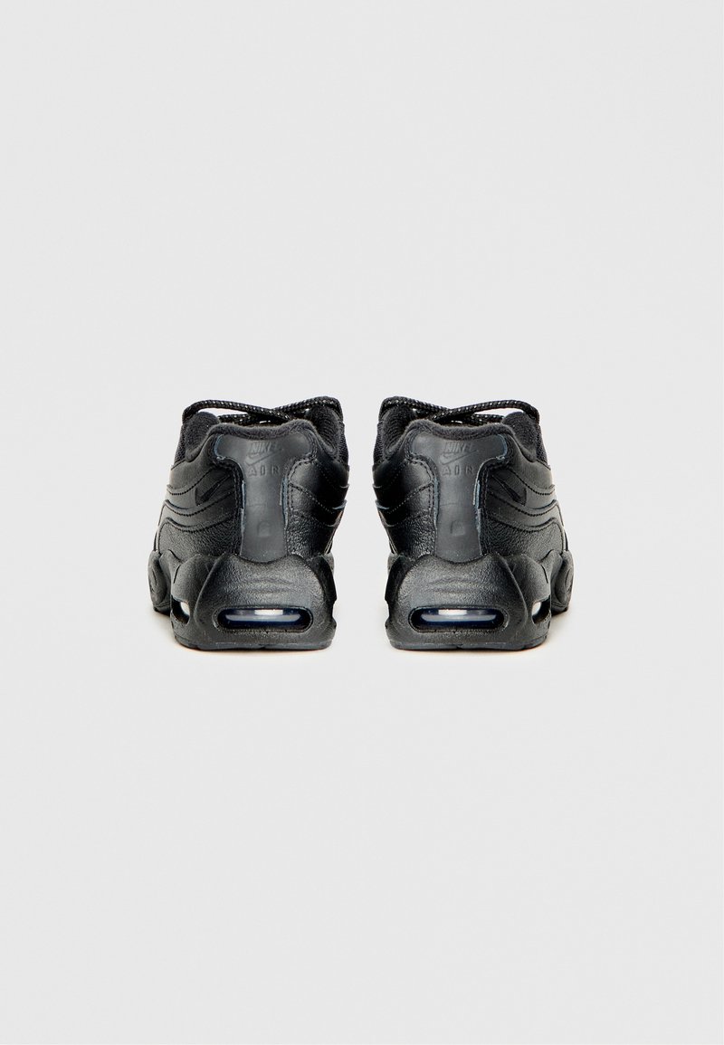 Une paire de baskets Nike Air Max noires vues de l'arrière sur un fond gris clair uni.