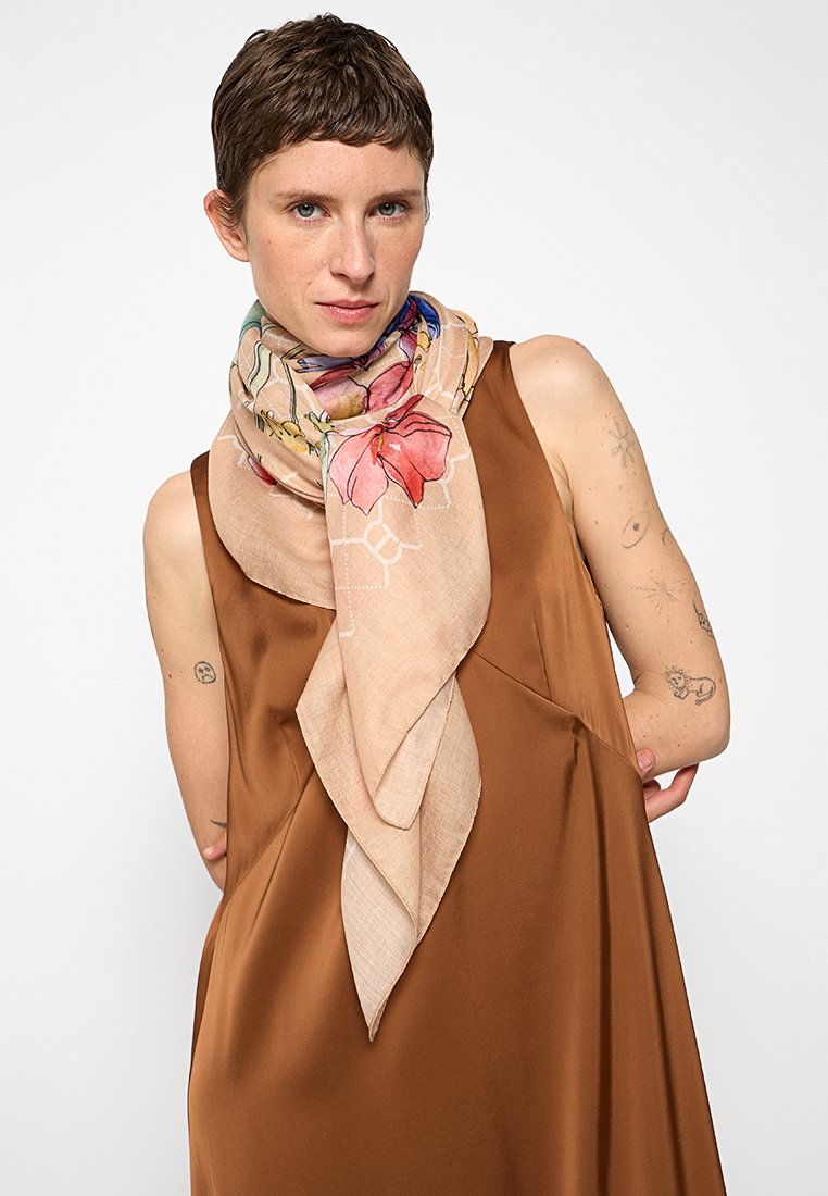 Leichter beiger Schal mit floralen Mustern, elegant um den Hals drapiert. Der Stoff hat eine weiche Textur und eine dreieckige Form.