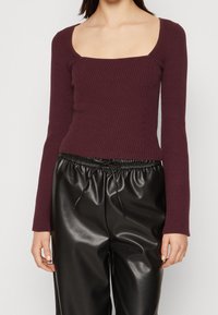 Bordowa prążkowana bluzka z długim rękawem i kwadratowym dekoltem, zestawiona z czarnymi, wysokim stanem spodniami z eko skóry z elastycznym sznurkiem w talii.