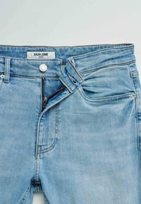 Light blue skinny jeans with unzipped fly, buttoned waistband, front pockets, and visible "Salsa Jeans" brand label inside.