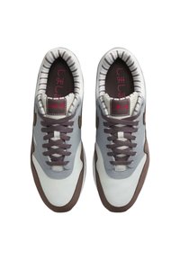 Białe i szare trampki z brązowymi akcentami, siateczkowym językiem i teksturowanymi sznurówkami. Wnętrze ma paskowaną grafikę i czerwony napis.