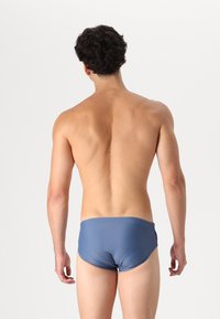 Swim briefs in dark blue fabric, featuring a seamless waistband and a snug fit. The design is minimal with no visible logos or patterns.