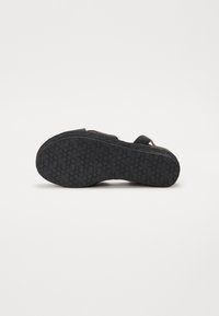 Die schwarze Sandalensohle weist eine strukturierte GummOberfläche mit Sternmustern auf. Ein gewebter Jute-Einfassung umrandet die Kante für zusätzliche Details.