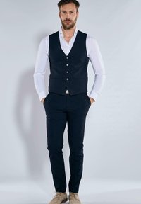 Marineblauer, maßgeschneiderter Westen über einem weißen Hemd, kombiniert mit passenden Hosen. Verfügt über fünf Knöpfe, schmale Passform und minimalistisches Design.