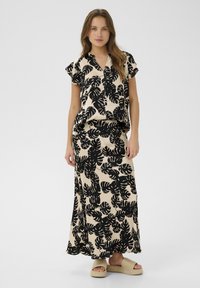 Fekete és bézs két részes szett, amely egy rövid ujjú, gombos ingből és egy hosszú szoknyából áll, mindkettő trópusi levél mintázattal díszítve.