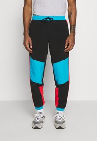 Pantalones de chándal negros con paneles azules y rojos, cinturilla elástica y puños. Hechos de material suave, con bolsillos laterales y un corte holgado.