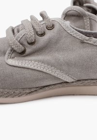 Gray canvas shoe featuring round laces, bronze eyelets, and contrasting stitching, with a textured surface and a flexible sole.