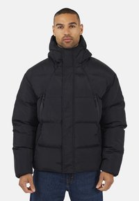 Veste rembourrée noire avec capuche, dotée d'une fermeture éclair, de deux poches zippées latérales et d'un design matelassé. Texture douce, isolation chaude.