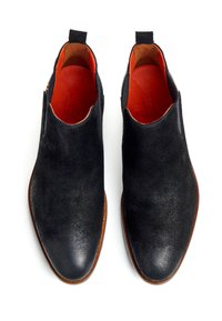 Bottines Chelsea en suede noir avec un bout lisse, intérieur orange contrastant et semelle en cuir marron. Dotées de panneaux latéraux élastiques et d'une languette à l'arrière.