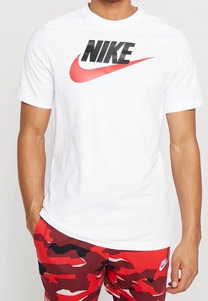 Mann trägt weißes Nike-T-Shirt mit schwarzem und rotem Logo, kombiniert mit roten Camouflage-Nike-Shorts.