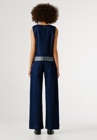 Tumesinine denimikomplekt, mis sisaldab ilma varrukateta toppi ja laia jala pükse. Metallik hõbedane vöökoht pükstel ja madalad kingad.