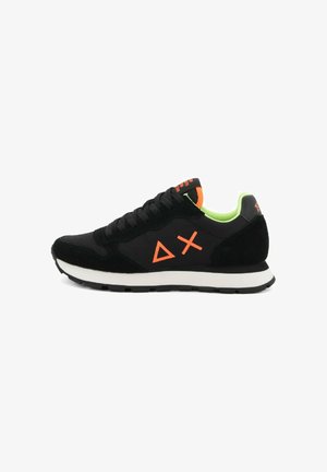 Zapatilla negra con forro interior verde neón, triángulos naranjas y símbolos de cruz en el costado, media suela blanca y suela exterior negra.