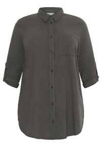 Chemise boutonnée vert foncé, manches longues retroussées aux coudes, poche poitrine unique, tissu lisse et ourlet arrondi.