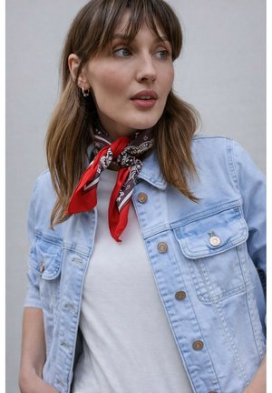 Mladá žena s hnědými vlasy, která nosí červený šátek se vzorem kolem krku, bílou košili a světlomodrou džínovou bundu, hledící stranou.