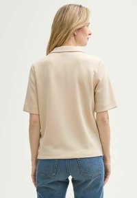 Polo de manga corta beige, textura suave, cuello clásico, ajuste sutilmente entallado, combinado con jeans de mezclilla azul.