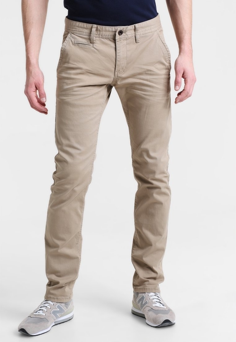 Pantalons en coton beige à coupe slim, avec poches avant et arrière et fermeture à boutons. Portés avec des baskets gris clair.