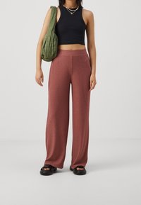 Pantalons larges côtelés en rose pâle, associés à un débardeur noir court. Un sac à épaule matelassé vert olive et des sandales noires complètent le look.