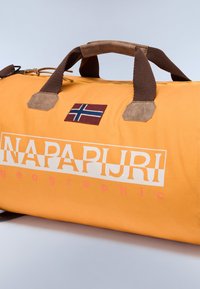 Borsa a tracolla arancione con manici marroni, dettagli in camoscio e una patch con la bandiera norvegese. Presenta un evidente marchio in testo bianco. Texture liscia.
