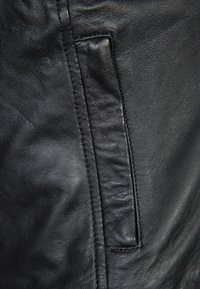 Black leather with a smooth texture, featuring a vertical pocket with a subtle stitch detail. The design shows slight variations in surface sheen.